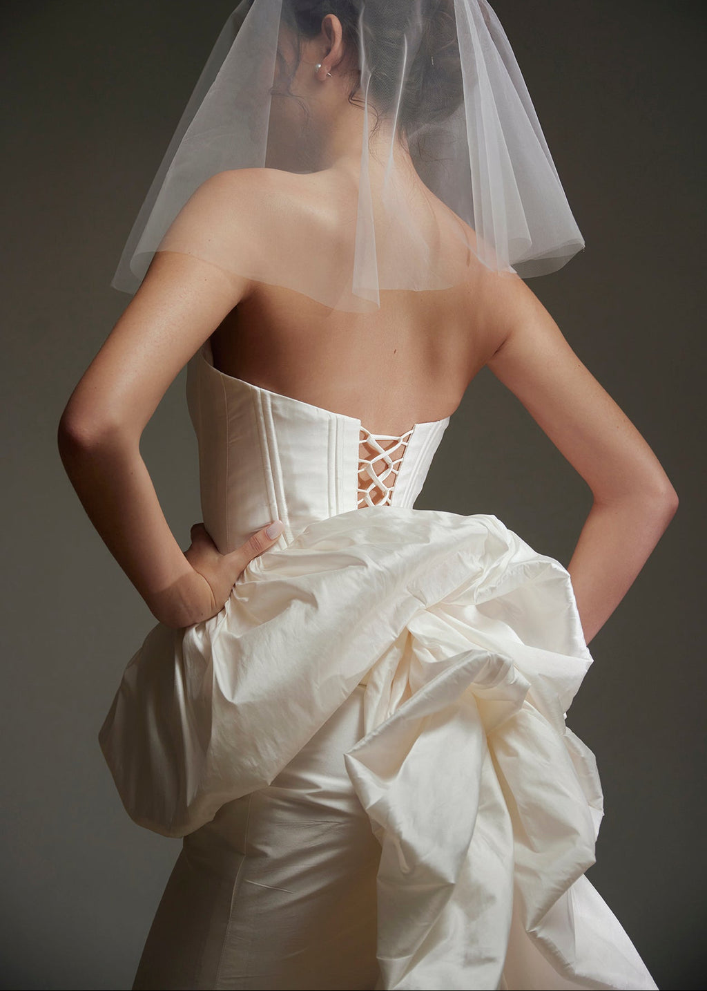 Woman wearing a white wedding dress with a sheer veil against a dark background