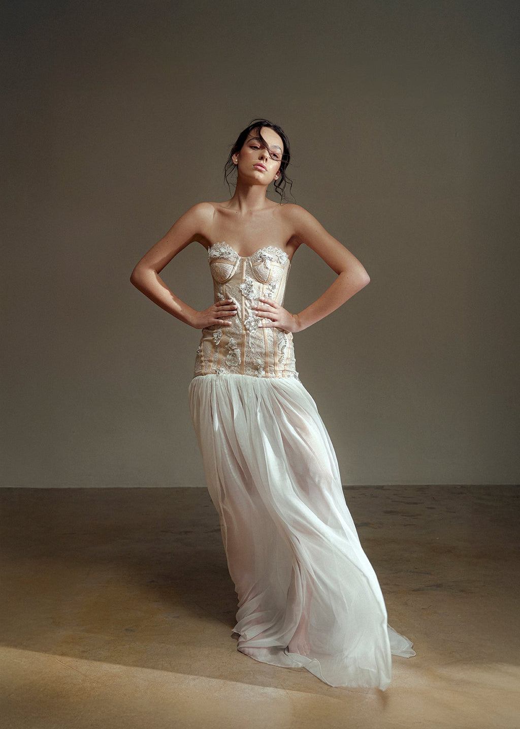 Woman wearing a strapless top and flowing white skirt against a plain background