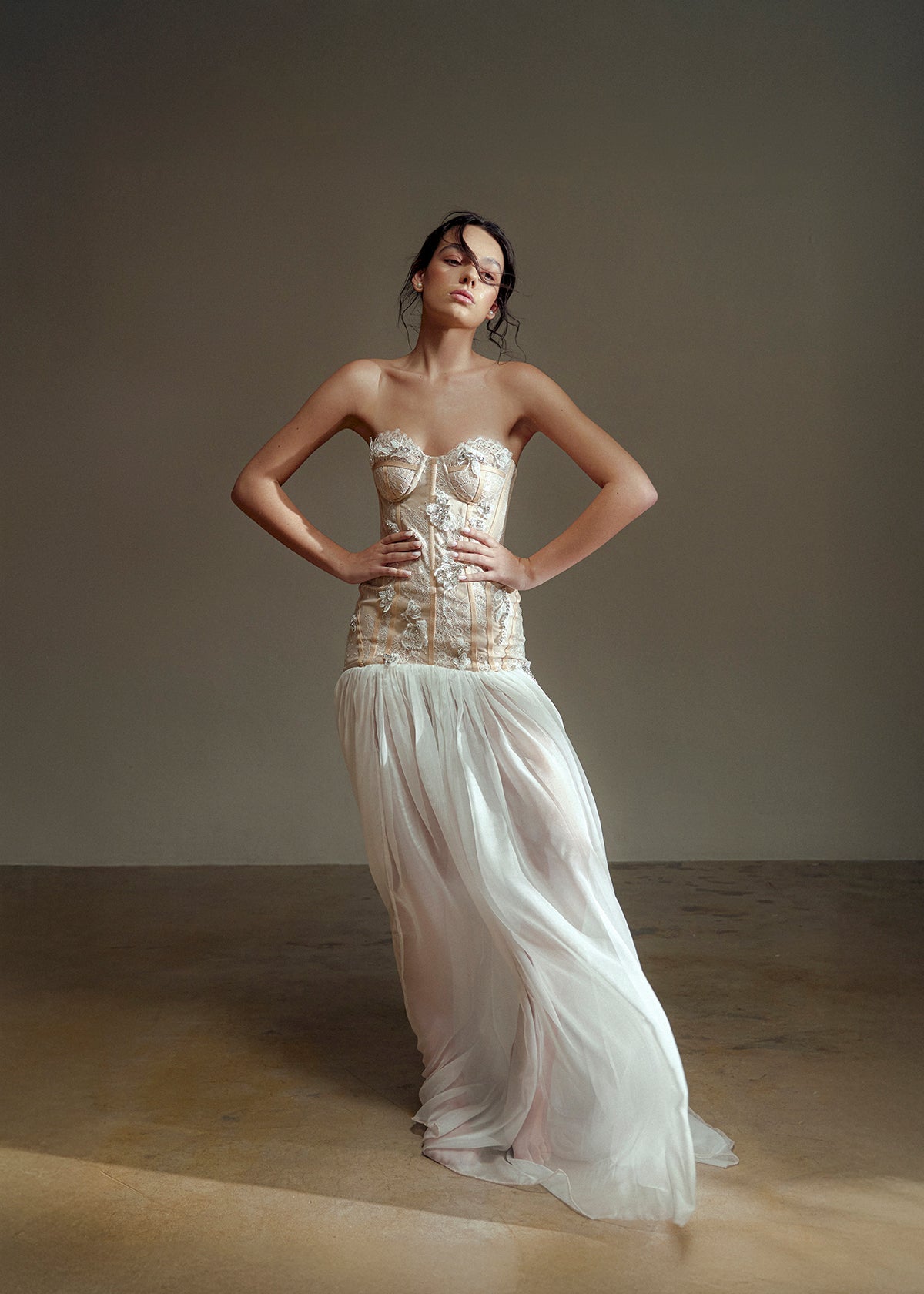 Woman wearing a strapless top and flowing white skirt against a plain background