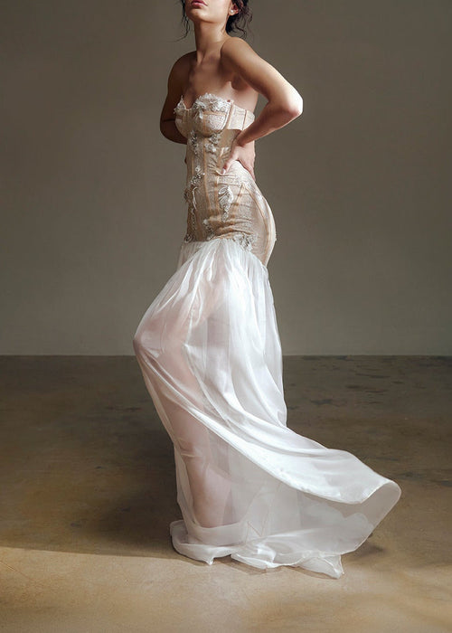 Woman in a white strapless gown standing against a plain background