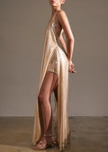A model wearing a shimmering metallic champagne-gold halter maxi dress with a high thigh slit, standing in a studio with a neutral gray background.