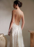 Woman wearing a white lace wedding dress with an open back, standing against a neutral wall.