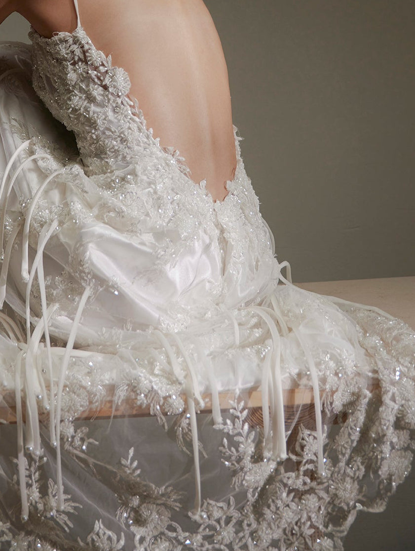 Person wearing a white lace dress sitting on a wooden bench against a plain background