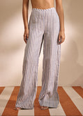 A model wearing high-waisted, wide-leg trousers with vertical blue and white stripes, paired with a cream bikini top, standing against a beige wall on a striped floor.